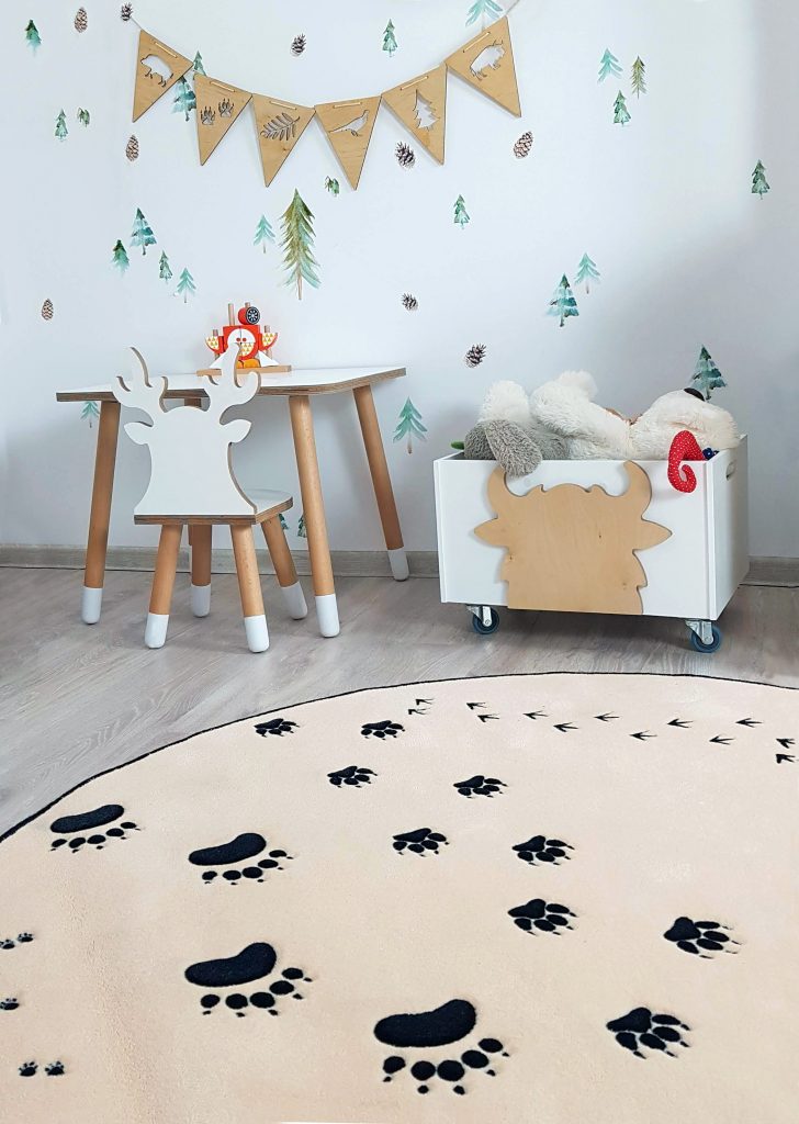 kącik pokoju dziecięcego, na środku podłogi leży waniliowy dywan w łapki zwierzat, pod scianą stoi biały stoliczek z krzesełkiem w kształcie jelonka